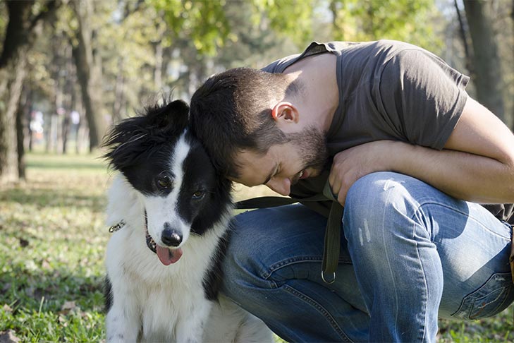 Man snuggling with a Border Collie outdoors.