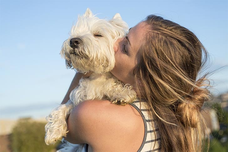 Woman holding and kissing a West Highland White Terrier.