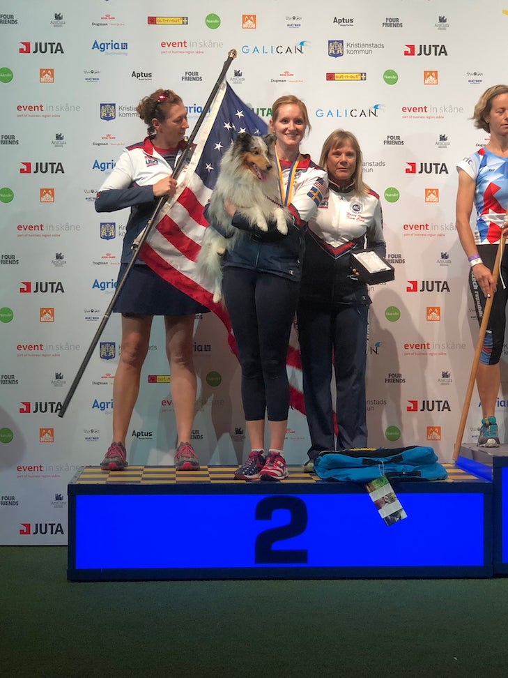 Jennifer and Swift stand on the awards podium after winning a silver medal at the FCI World Agility Championship.