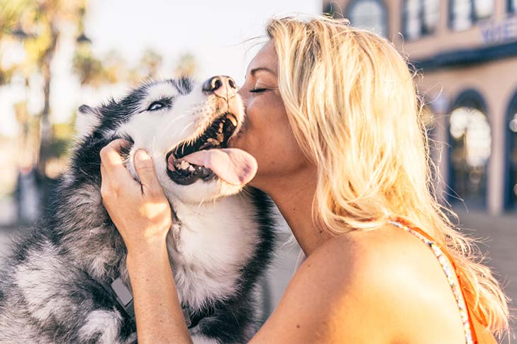 Woman kissing dog outdoors in sunshine.