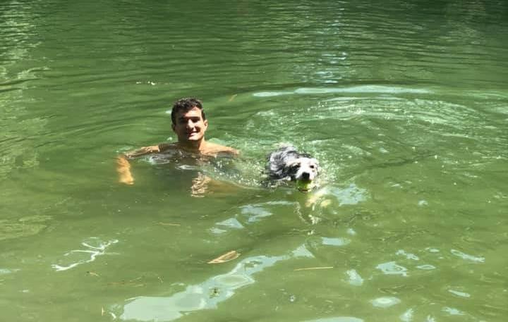 Dog and human swimming in a lake with a tennis ball.