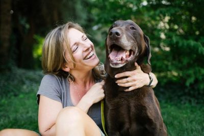 Labrador retriever being hugged by a woman sitting next to it.